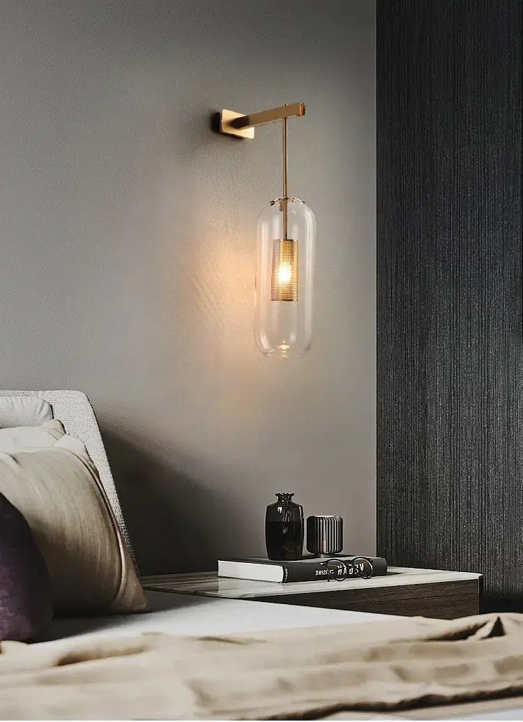 A sleek brass wall sconce with a clear glass lampshade featuring an illuminated bulb designed for nordic modern decor bedroom use.