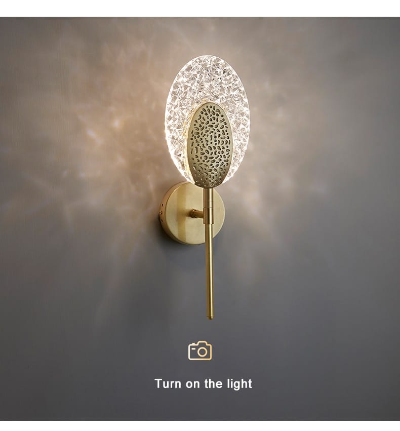 Gold-toned led wall lamp with textured oval-shaped glass diffuser and intricate metal cutout pattern for indoor lighting in bedroom.