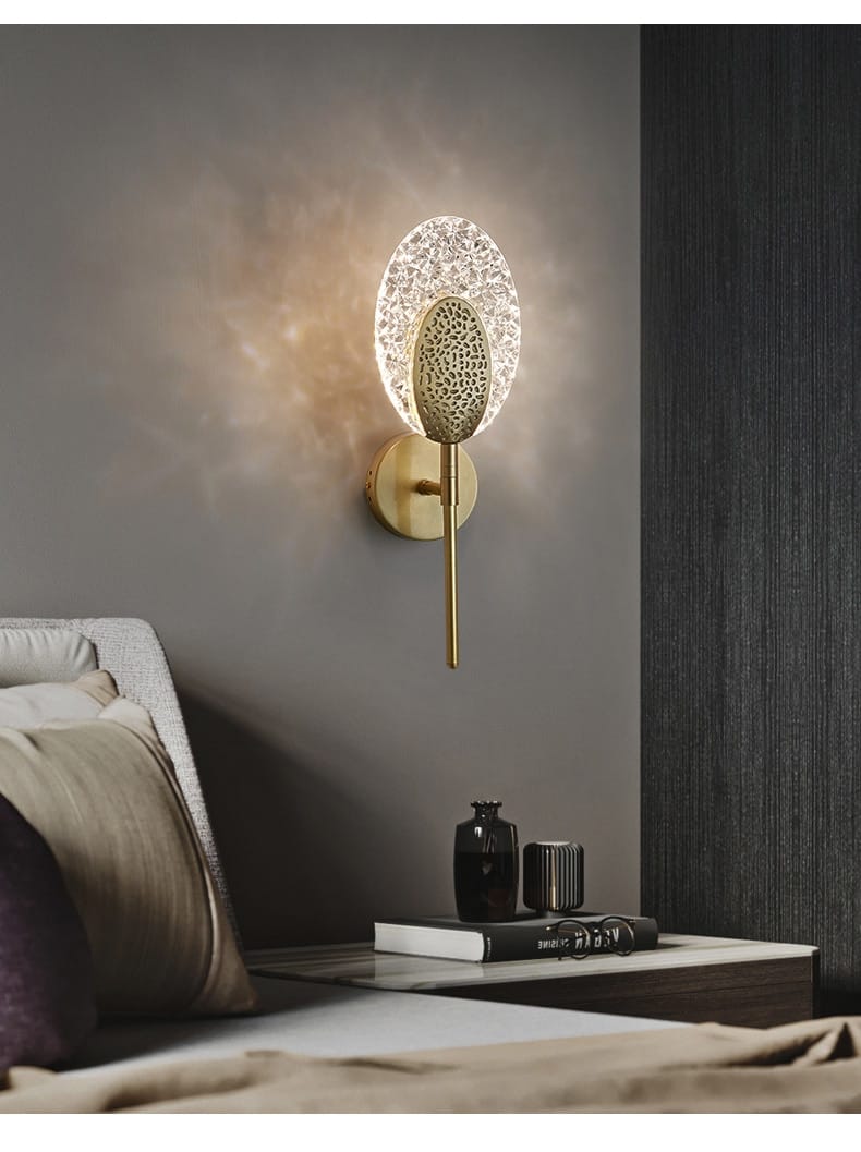 Gold-toned led wall lamp featuring a circular textured glass shade and an oval patterned metal accent for indoor lighting in the bedroom.