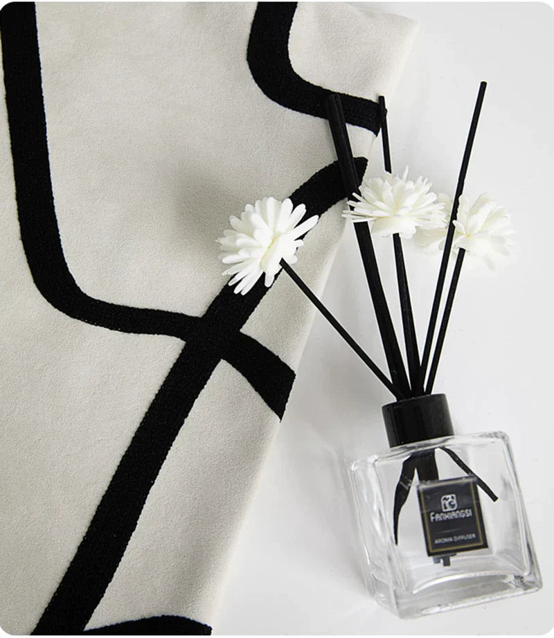 Funda de almohada bordada con líneas geométricas DecorBites™ en lona de ante negra, blanca y beige.