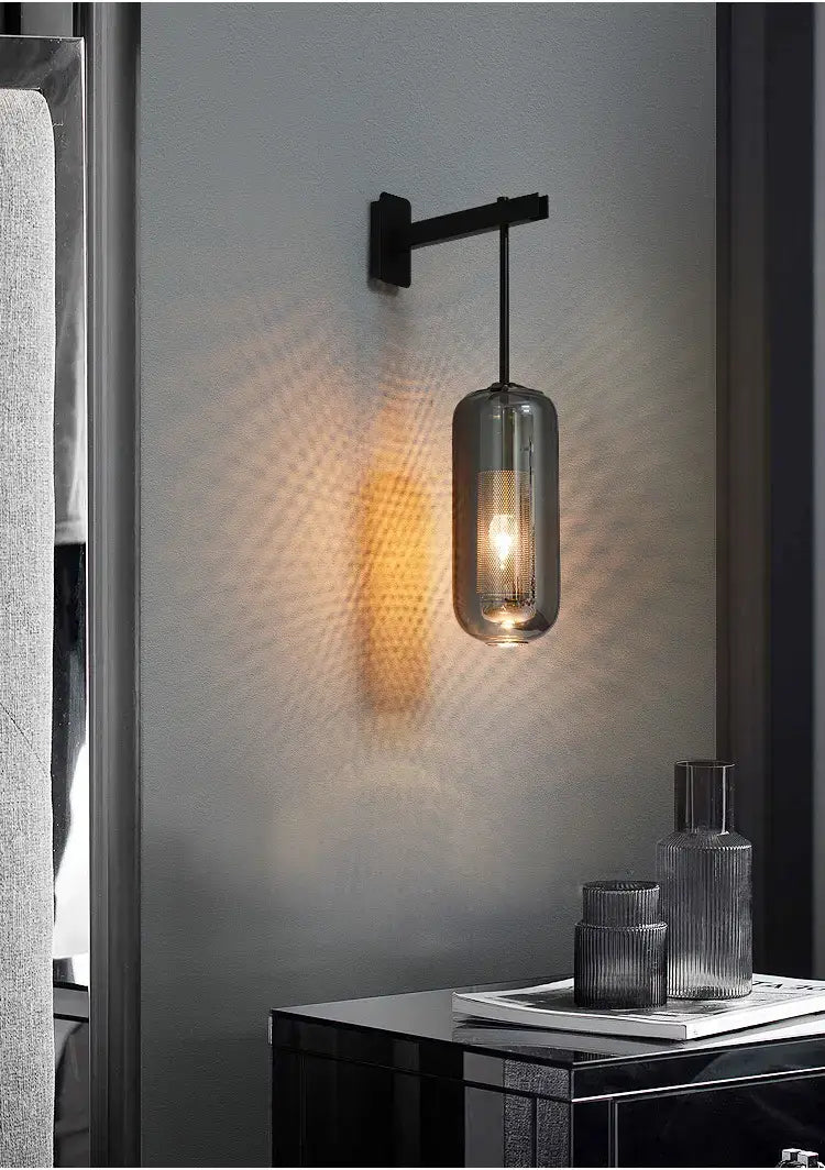 A nordic modern decor wall lamp featuring a sleek black metal arm and a cylindrical smoked glass lampshade with an exposed bulb, ideal for bedroom modern decor glass lighting.