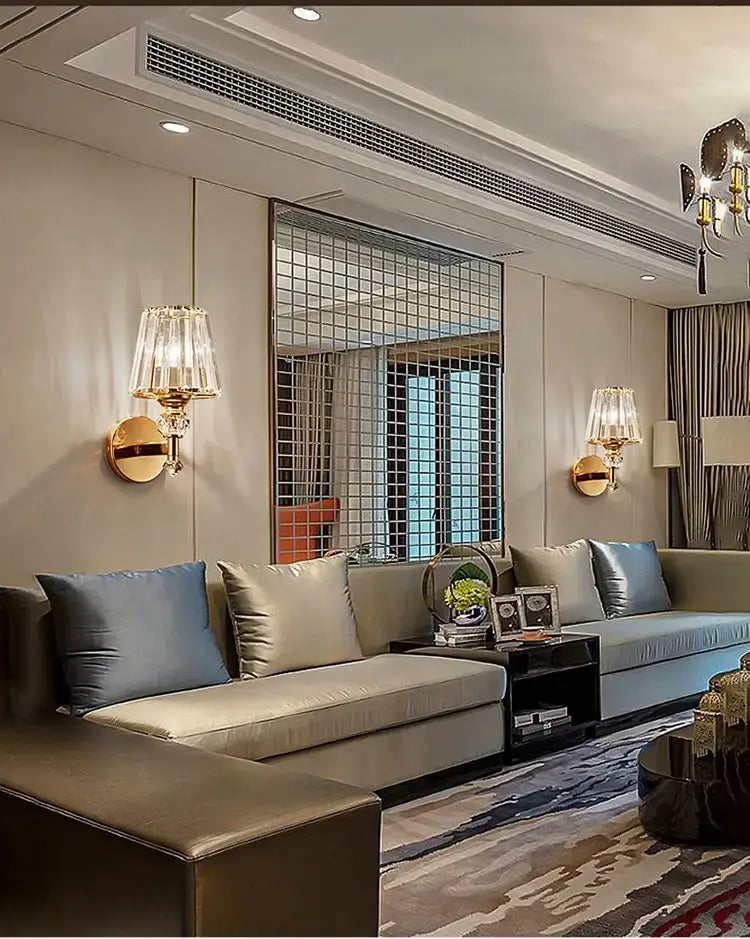 beige leather sectional sofa with blue and gray throw pillows beside a modern minimalist gold wall lamp with crystal shade for bedroom use