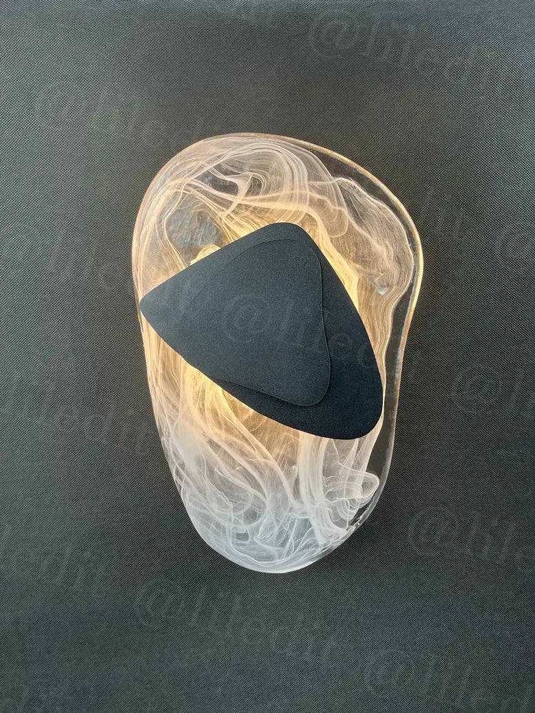 A modern creative minimalist translucent glass wall lamp with a swirling body and an embedded black triangular accent designed for bedroom bedside lighting.
