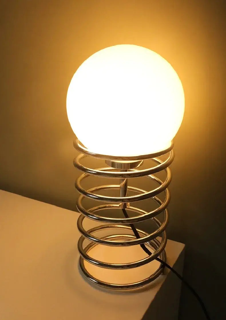 Warm-toned spherical white glass bauhaus spring table lamp with polished chrome spring base ideal as a bedroom light.