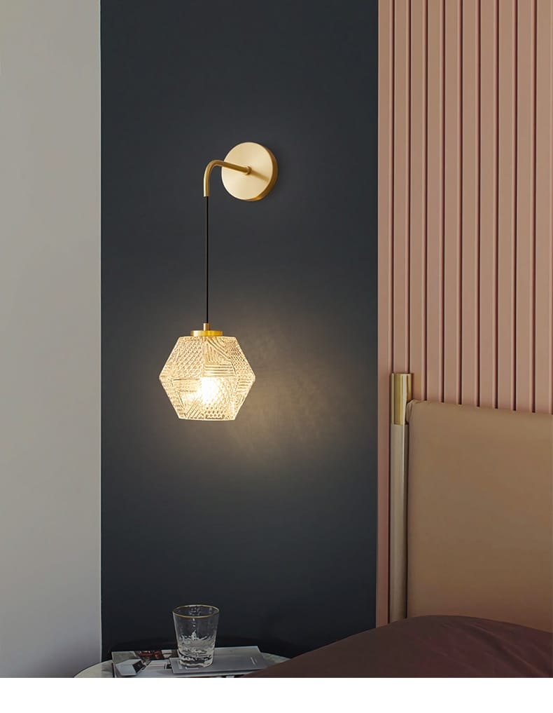 a hexagonal glass postmodern luxury led wall lamp with a gold-toned metal frame and intricate etched patterns, suspended from a curved brass wall mount for bedroom lighting