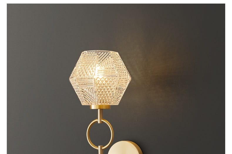 A hexagonal faceted glass lampshade with a gold-toned metal base and ring in a nordic postmodern luxury led wall lamp for bedroom lighting.