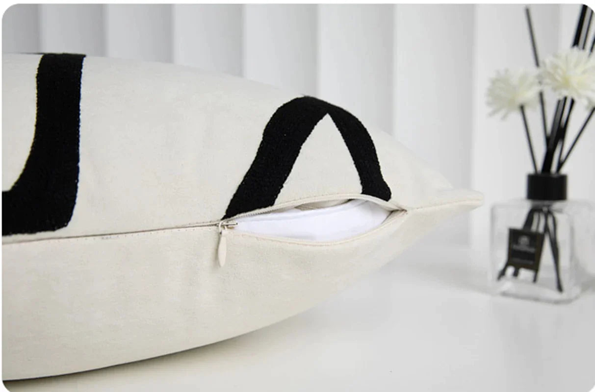 Funda de almohada bordada con líneas geométricas DecorBites™ en lona de ante negra, blanca y beige.