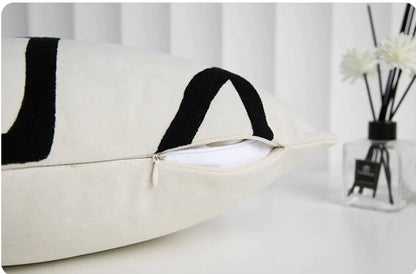 Funda de almohada bordada con líneas geométricas DecorBites™ en lona de ante negra, blanca y beige.