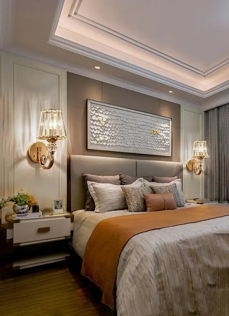 A modern minimalist wall lamp with a crystal shade in gold featuring a textured silver and gold metallic rectangular backplate with overlapping circular scales for bedroom use.