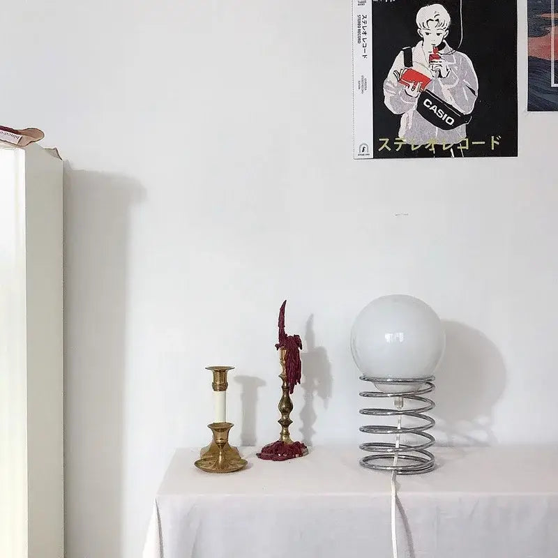 A bauhaus spring table lamp featuring a sleek chrome spring and a frosted white spherical glass shade designed as a bedroom light.