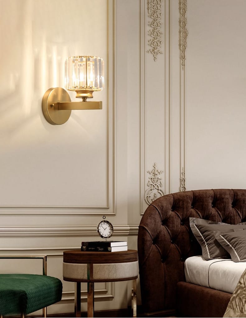 Modern minimalist wall sconce featuring a gold-toned frame with a faceted crystal glass shade for bedroom lighting.
