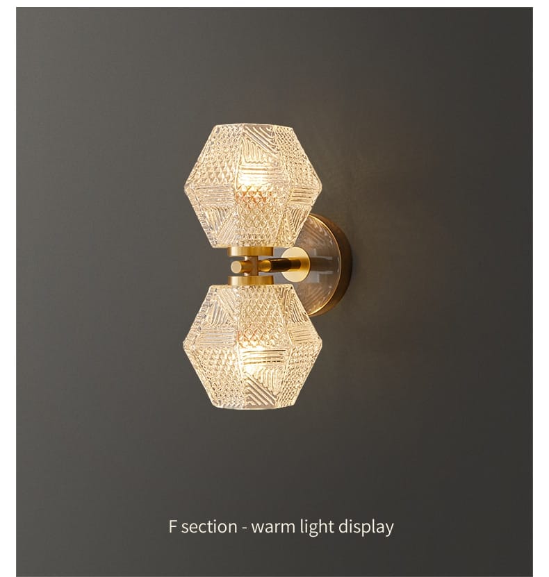 A warm-toned postmodern luxury led wall lamp featuring a hexagonal glass sconce with intricate cut patterns and a brass-finished metal base for bedroom lighting.