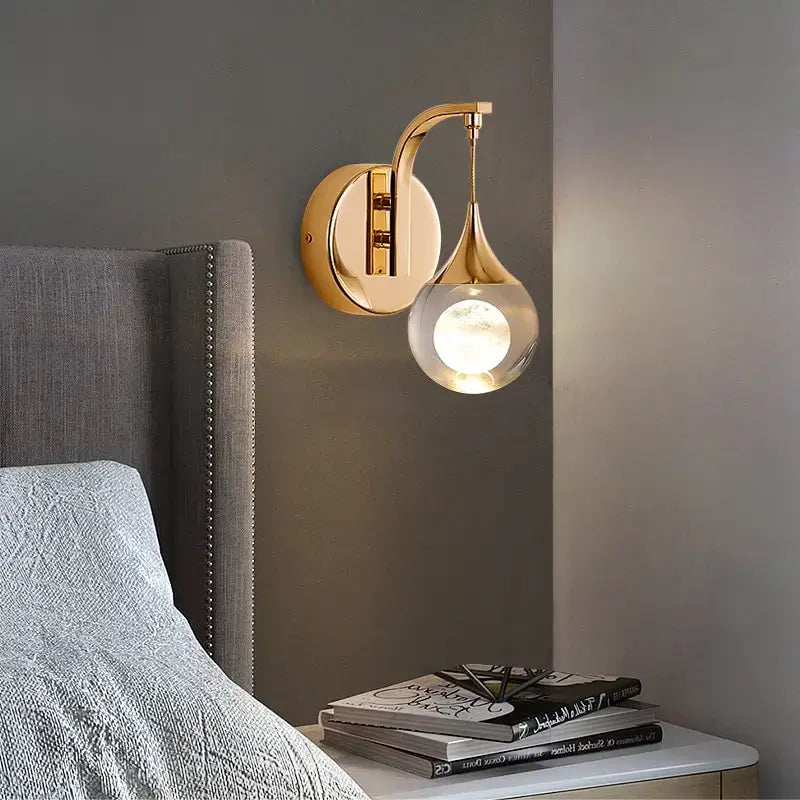 Modern luxurious crystal led wall sconce featuring a gold-toned curved lamp with a teardrop-shaped glass globe ideal for bedroom lighting.