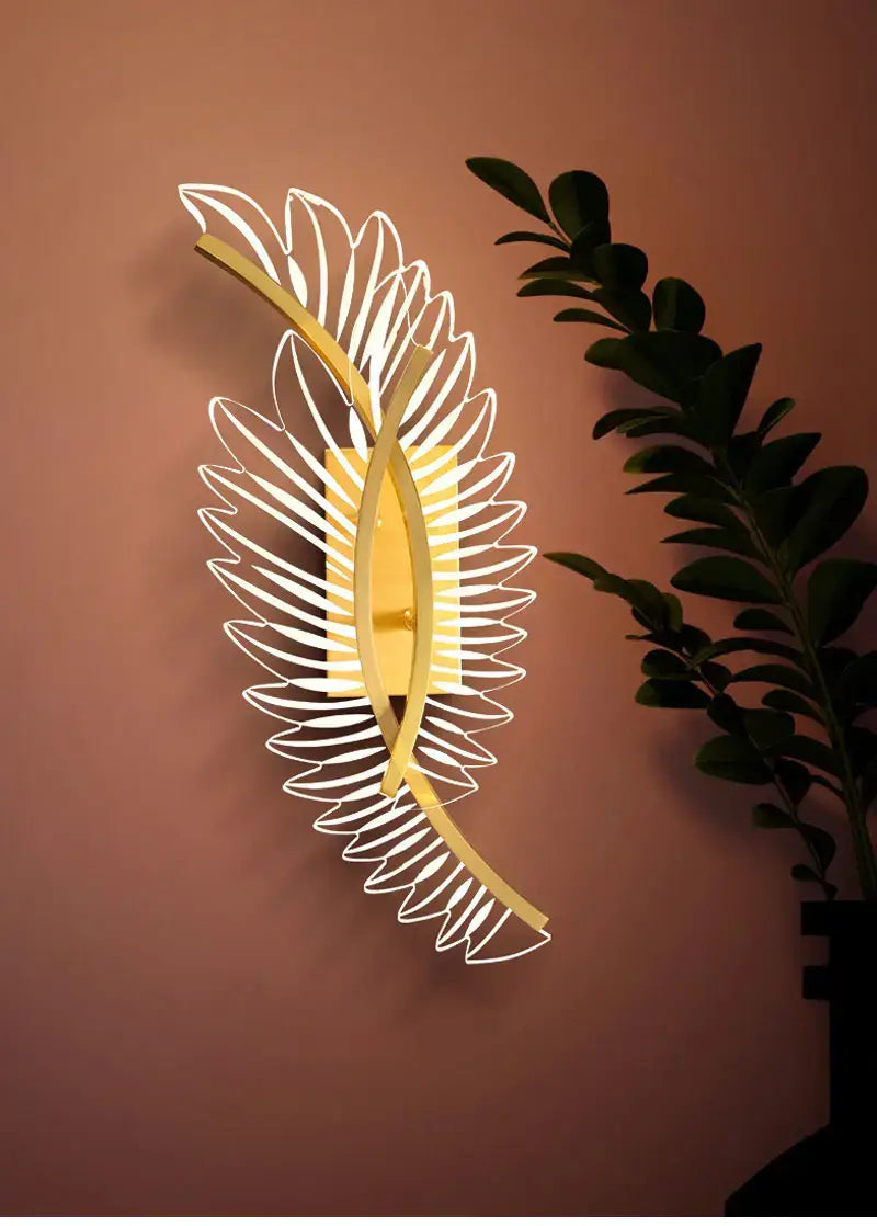 gold-toned feather-shaped wall lamp with sleek modern art design and illuminated center for nordic modern art bedside use