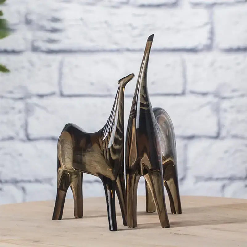 Two sleek minimalist giraffe figurines with reflective bronze finish decorbites horse couple sculpture set on wooden surface