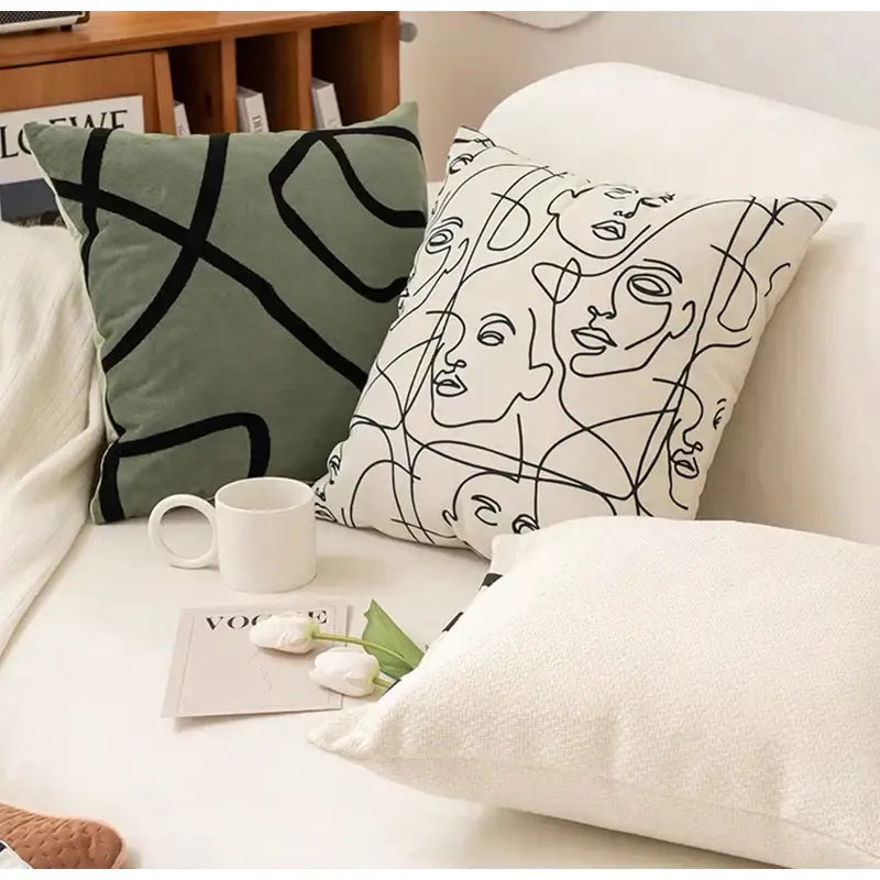 A decorbites beige textured pillow cover with a white cushion and minimalist black line art abstract faces design