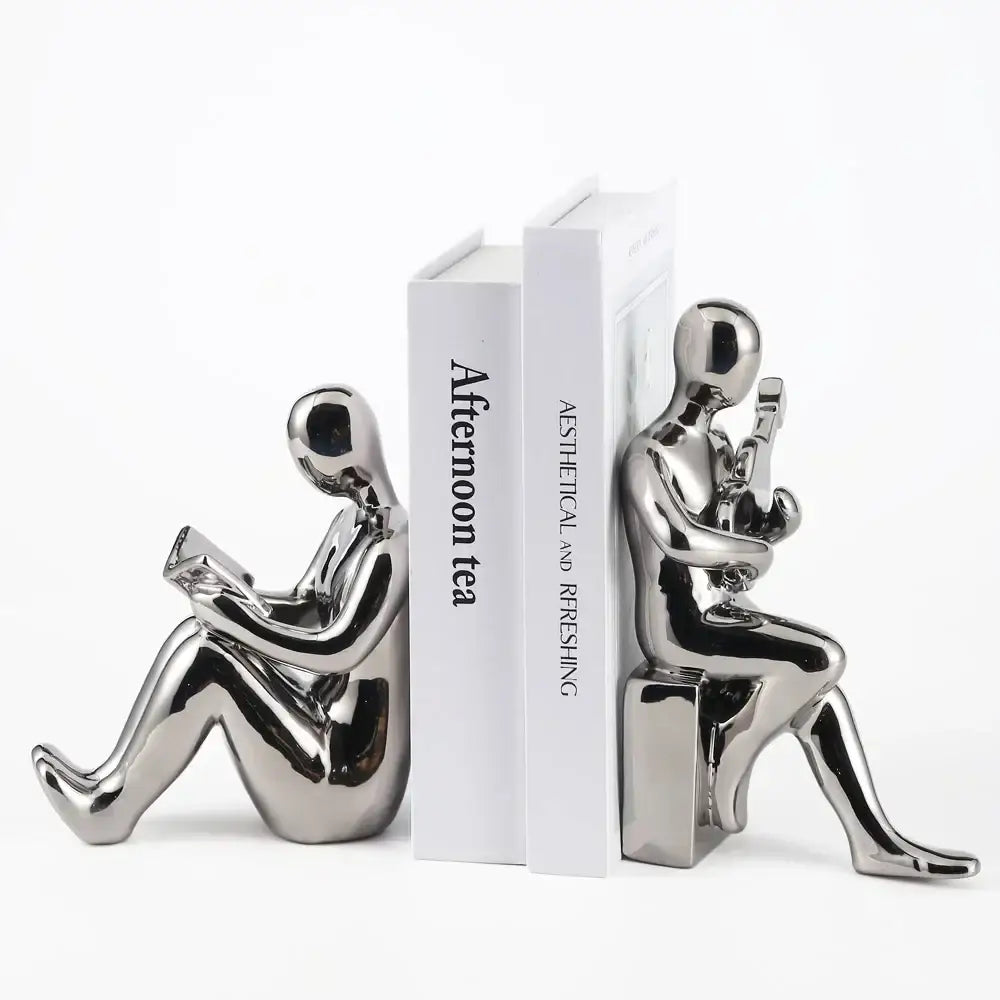 Shiny black and gold metallic character bookends shaped as seated figures reading and holding a phone in abstract nordic style