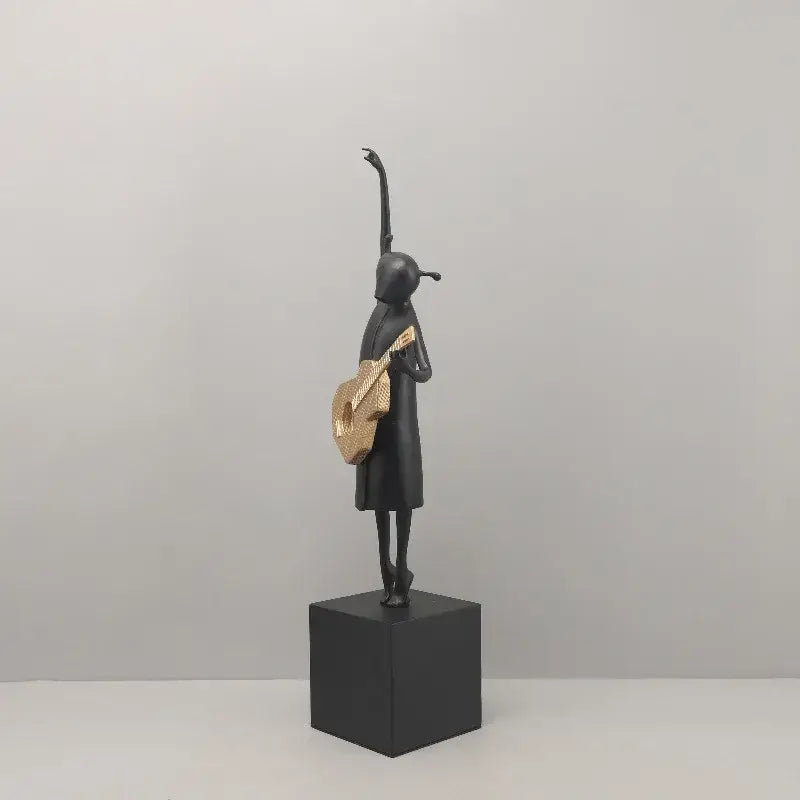 Abstract guitarist resin sculpture in black with gold-accented guitar standing on black cube base for living room decor