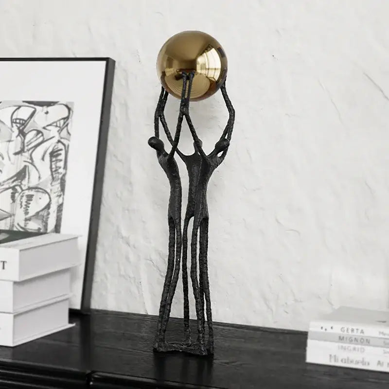 Abstract black sculpture of three intertwined figures supporting a polished golden ball holder for living room decor