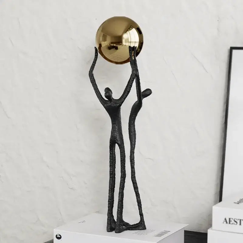Abstract black figurine with two elongated human forms supporting a reflective golden ball holder for living room decor