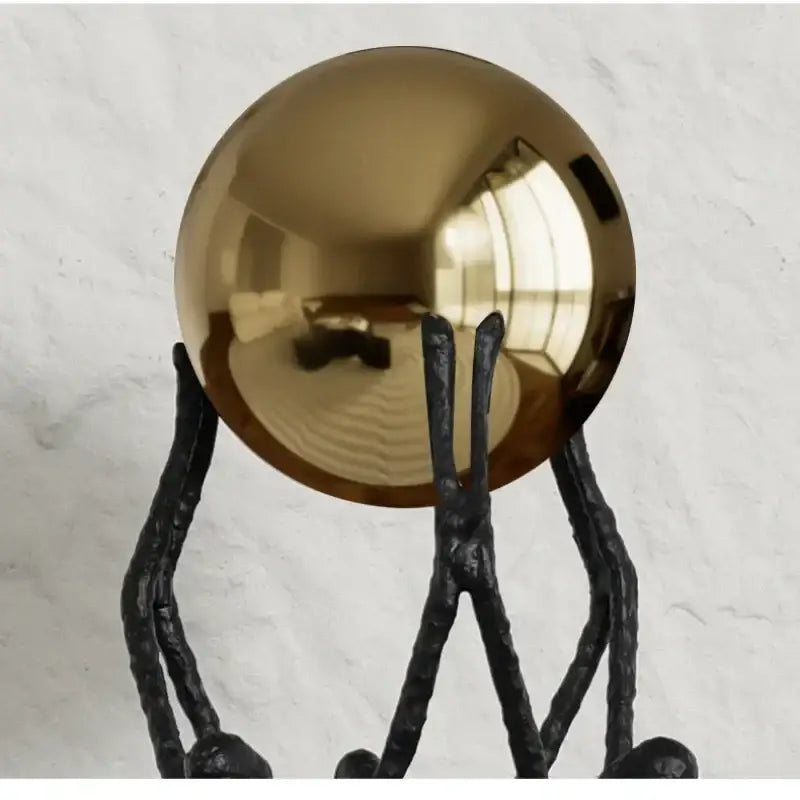 Shiny gold metallic sphere golden ball holder resting on black textured wrought iron stand for living room decor