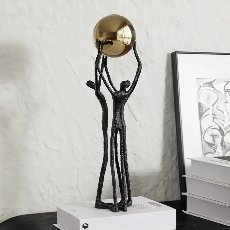 Black abstract figurine with two stylized human forms supporting a reflective golden ball holder for living room decor