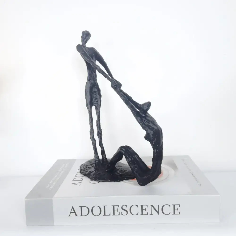 Black abstract hand dance sculpture of two intertwined figures on a book titled adolescence for living room decor