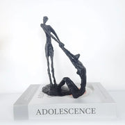 Black abstract hand dance sculpture of two intertwined figures on a book titled adolescence for living room decor