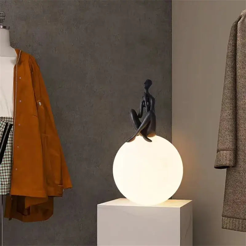Abstract black and red ball holding character resins lamp with a black sculpted figurine on a glowing white spherical lamp