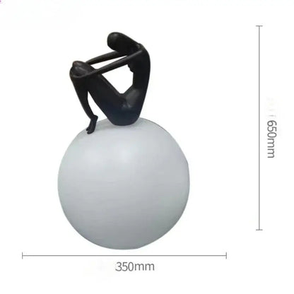 Black abstract ball holding character resin figurine seated on a matte white spherical base for living room decor