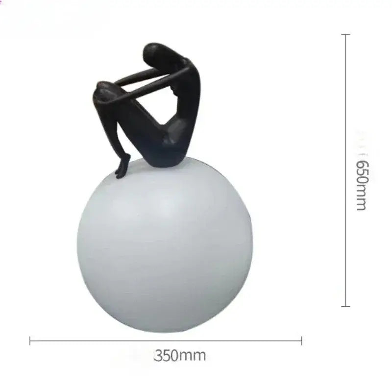 Black abstract ball holding character resin figurine seated on a matte white spherical base for living room decor