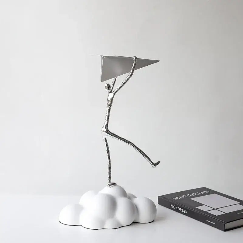 Silver metallic figurine holding a resin paper airplane on a white cloud base for living room decor