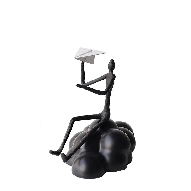 Black resin abstract figurine of a seated person holding a white resin paper airplane on a paper airplane cloud base
