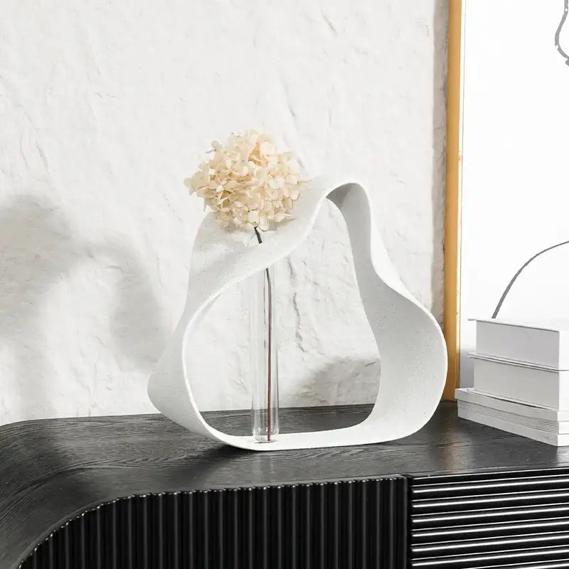 Abstract black resin ring sculpture featuring a white sculptural vase with glass stem and dried hydrangeas for home decor