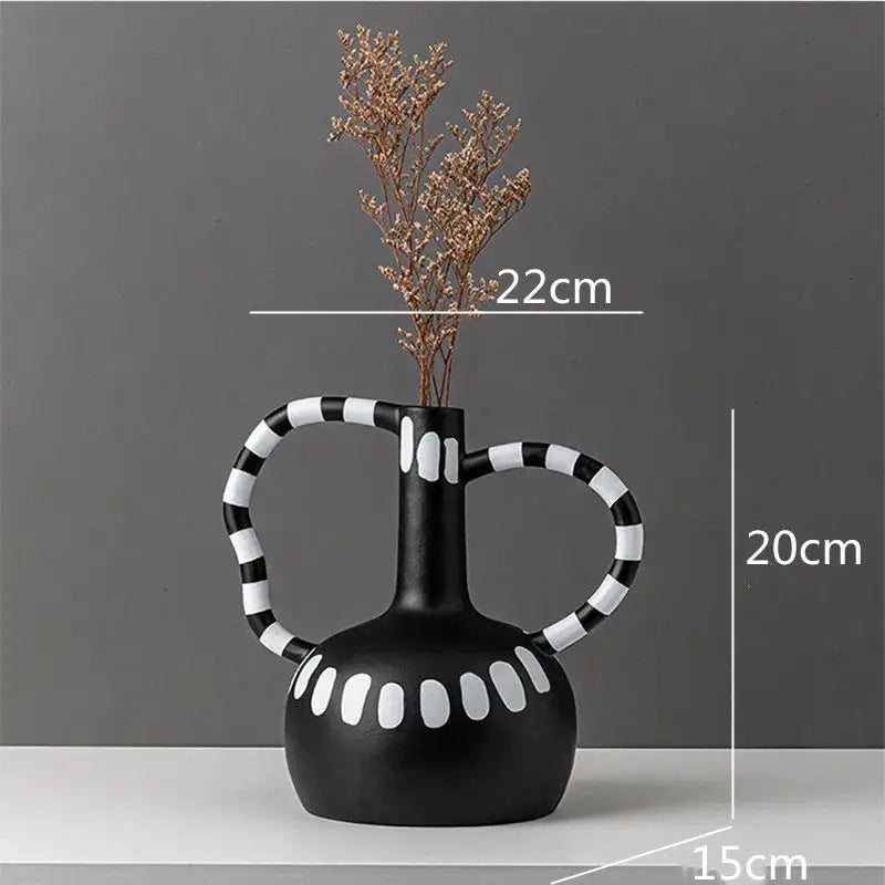 Abstract black and white ceramic vase with white spots and striped handles holding dried golden branches by decorbites ceramic