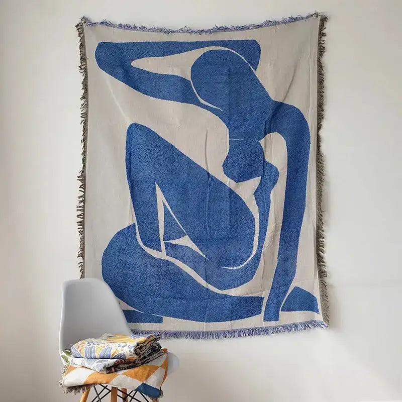 Beige throw blanket with bold blue abstract geometric knitted tassels and fringed edges hanging on wall