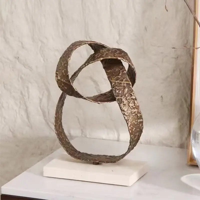 Bronze-colored textured metal geometric sphere pendant sculpture with interlocking loops on white marble base for decor