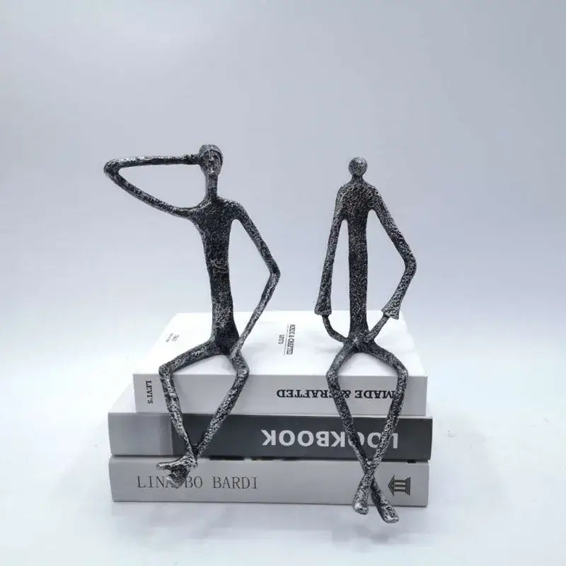 Two abstract bronze metal human sculptures in black textured finish sitting atop books for living room decorbites abstract metal decor