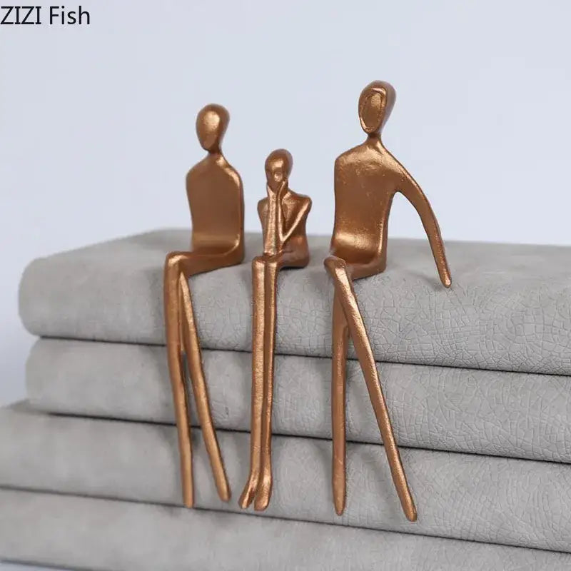 Bronze-colored abstract sculpture set with gold plated figure decor sitting on stacked gray fabric for living room