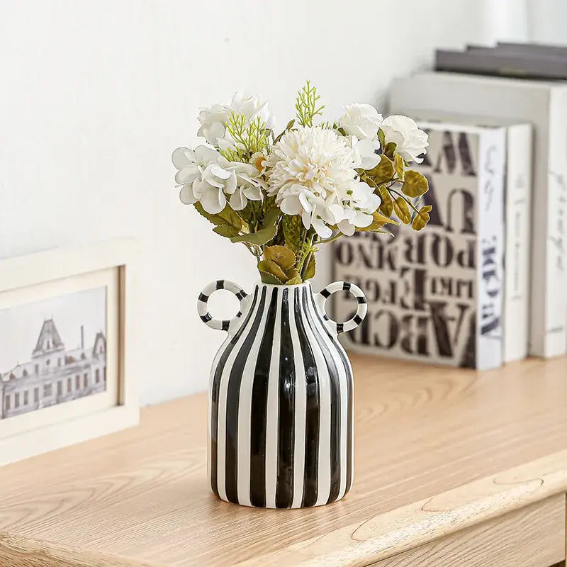 A sleek abstract ceramic hydroponic vase with bold black and white stripes and double ear handles holding white flowers