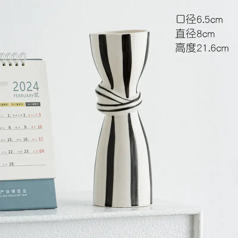 A sleek white abstract ceramic hydroponic vase with bold black stripes and a twisted band around its midsection
