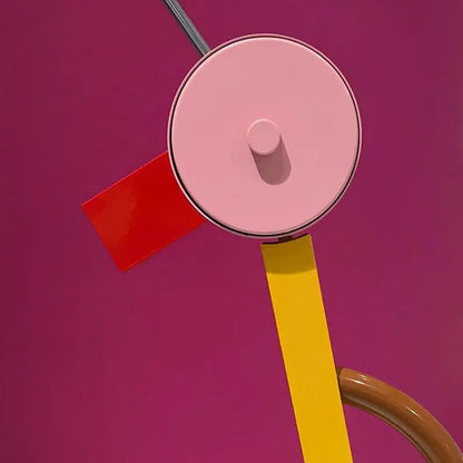Abstract duck led table lamp with a pink circular shade and metallic rim on a yellow arm against a magenta background