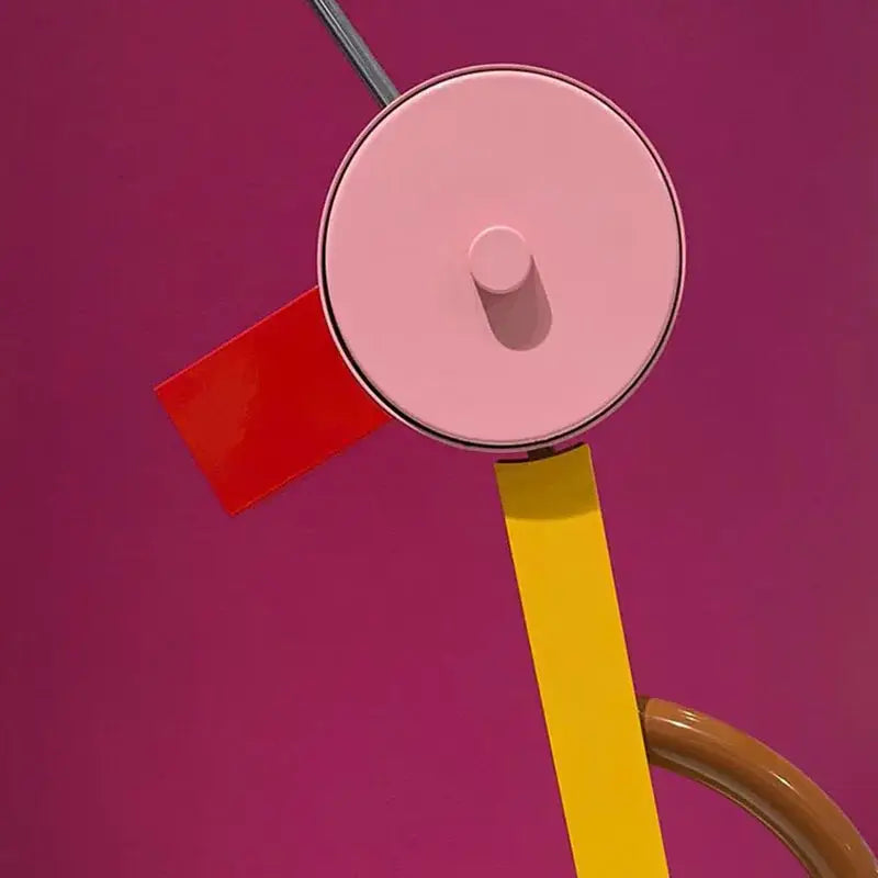 Abstract duck led table lamp with a pink circular shade and metallic rim on a yellow arm against a magenta background