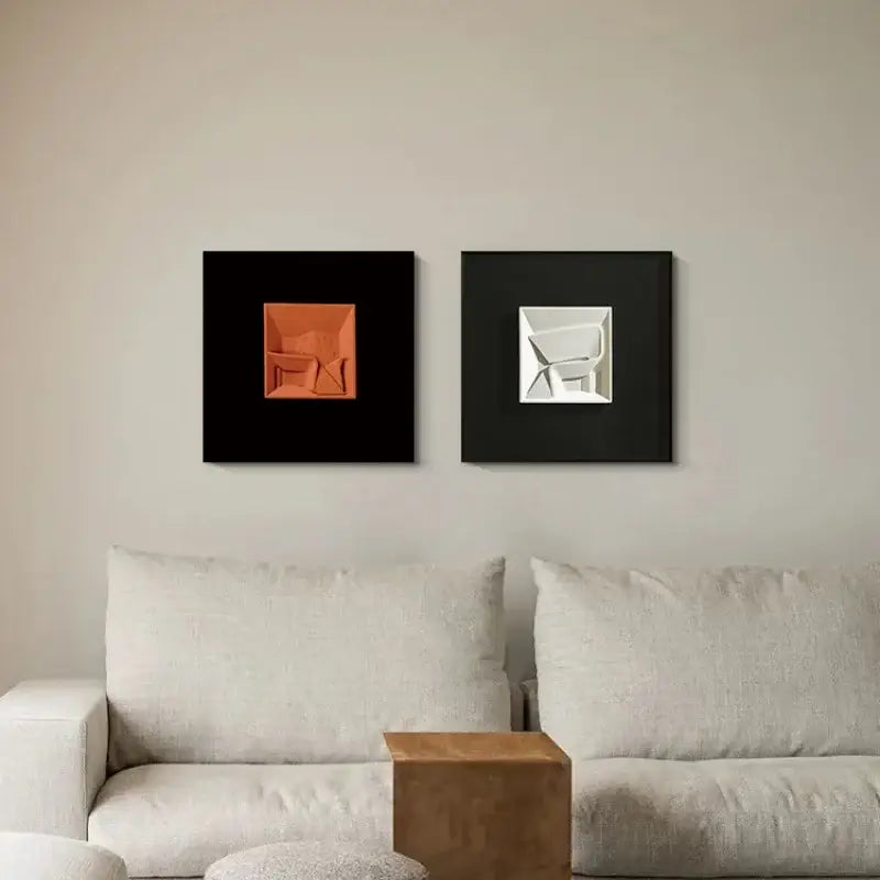 Two square-framed decorbites abstract geometric wall decorations featuring orange and white 3d sculptures on black backgrounds