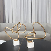 Two abstract gold line geometric metal sculptures with intertwined loops on white marble bases for living room decorbites decor