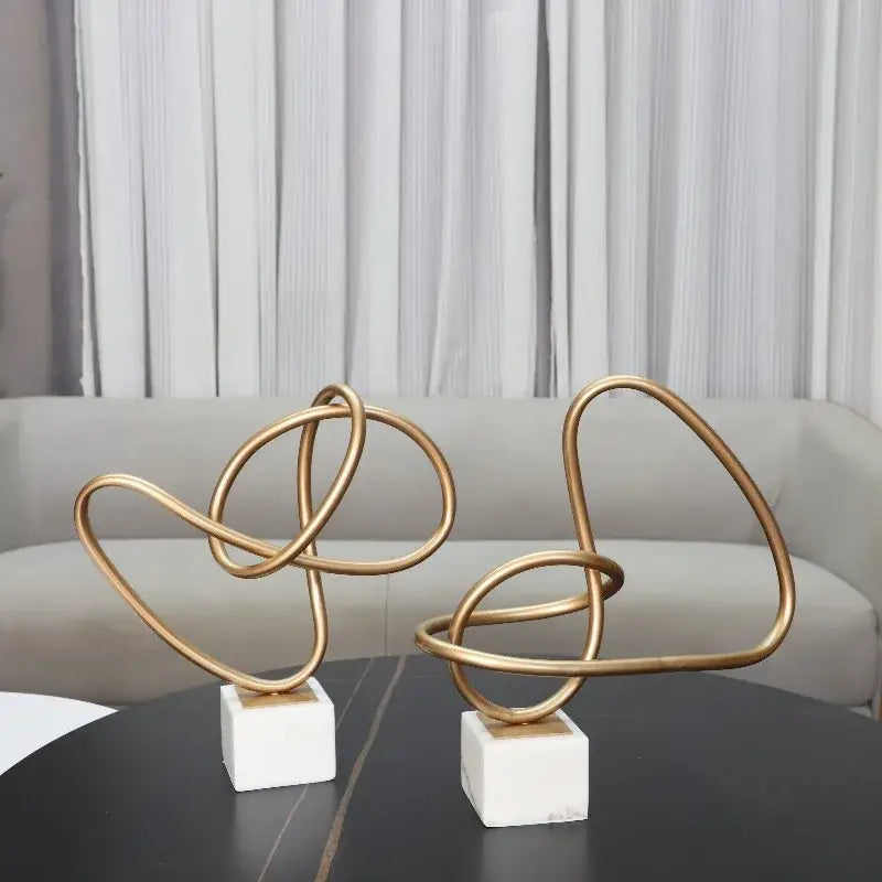 Two abstract gold line geometric metal sculptures with intertwined loops on white marble bases for living room decorbites decor