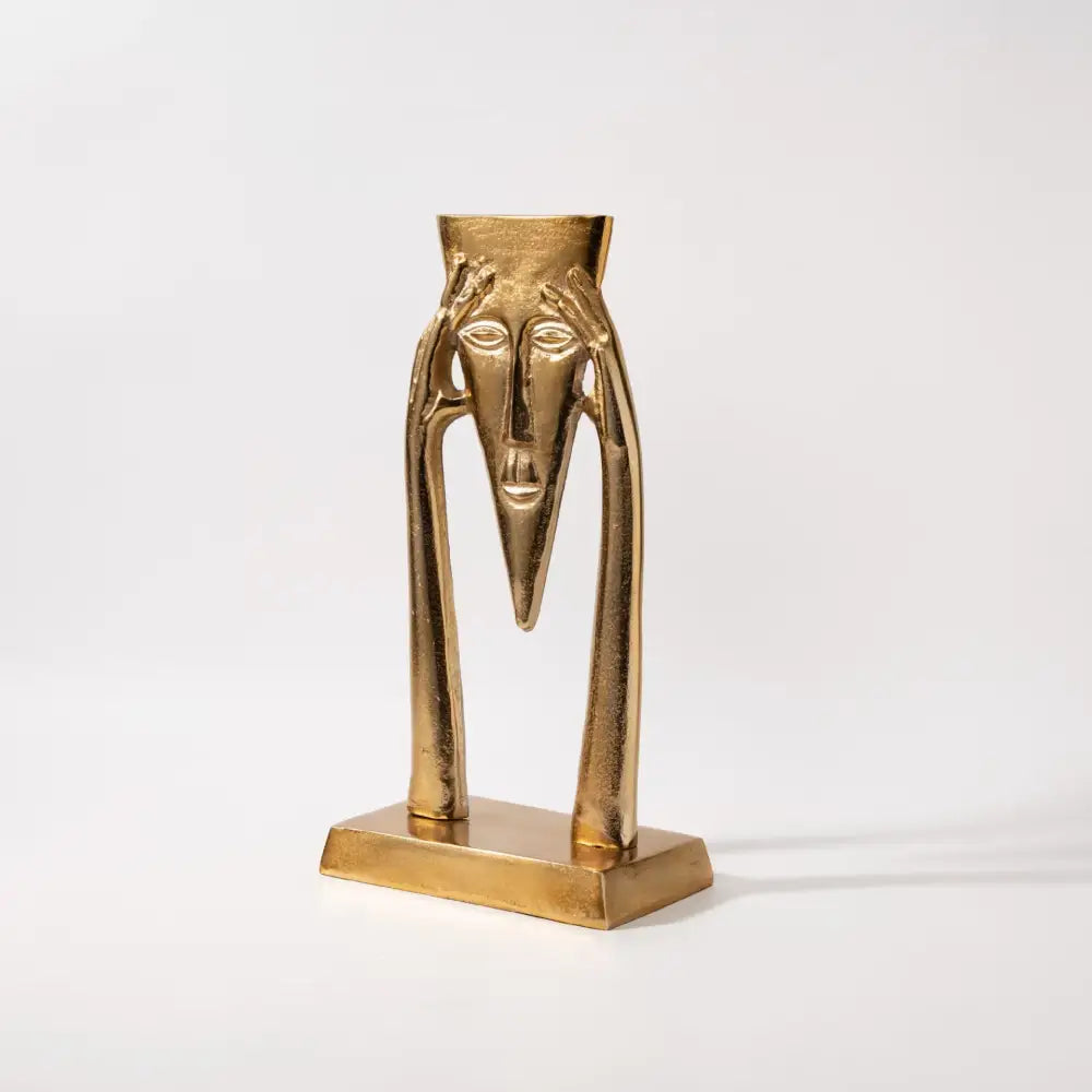 Abstract golden masked figure sculpture with elongated limbs and triangular nose on rectangular base for living room decor
