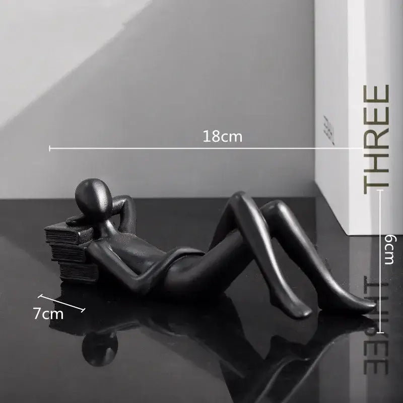 Black glossy resin figurine of a reclining human form on books as golden thinker reader man living room decor