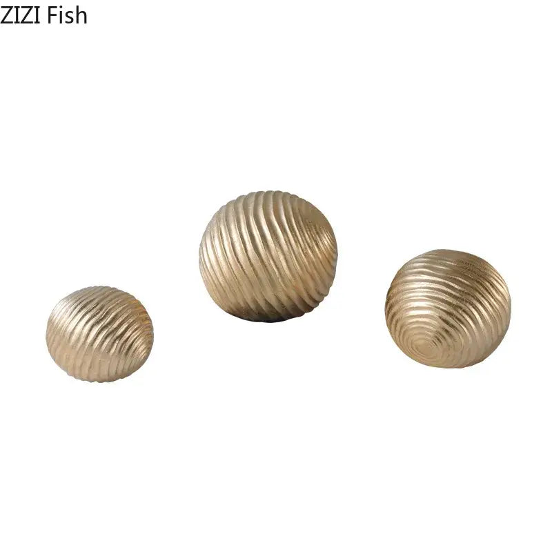 Set of three gold-toned ribbed metal decorative orbs for living room featuring an abstract golden wave ball design
