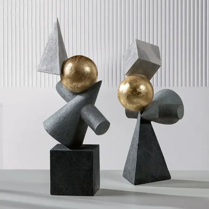 Two abstract gray resin sculptures with geometric gold ball accents on black bases for decorbites geometric gold decor